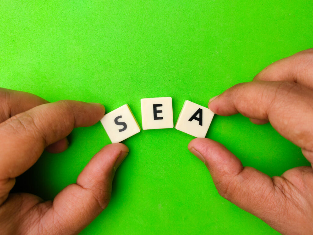 Top view hand holding toys letters with the word SEA on green background.
