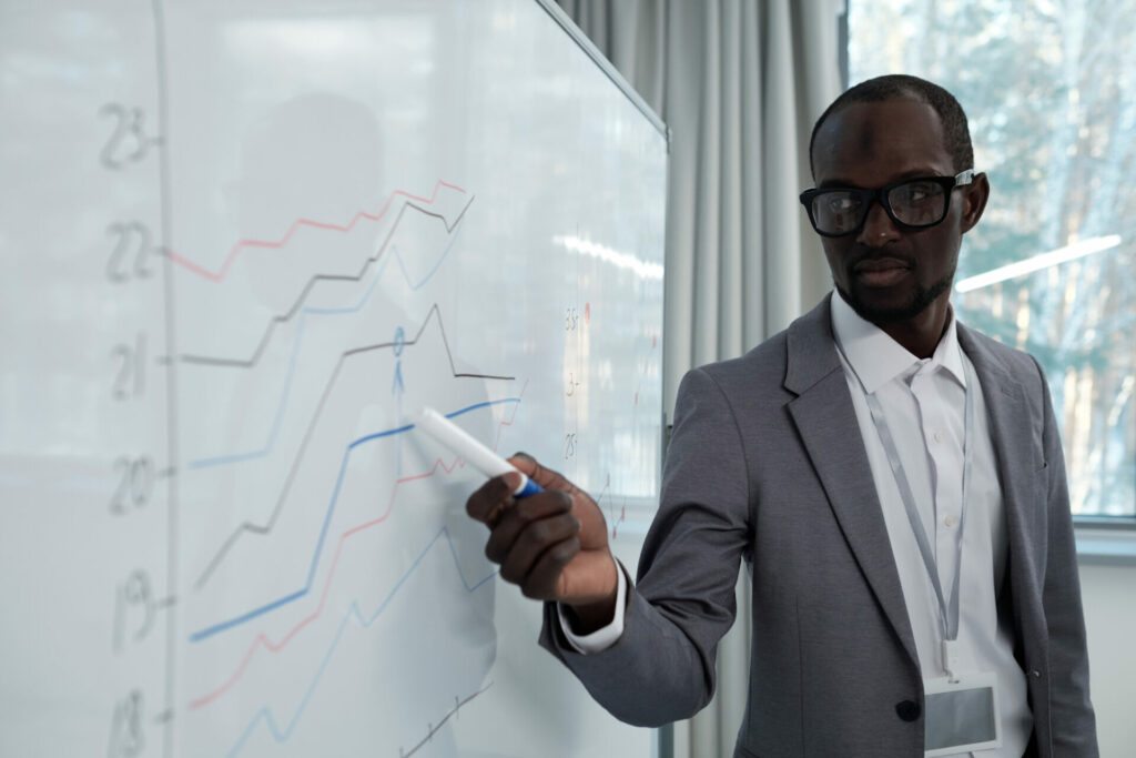 Young serious African American teacher pointing at graph on whiteboard